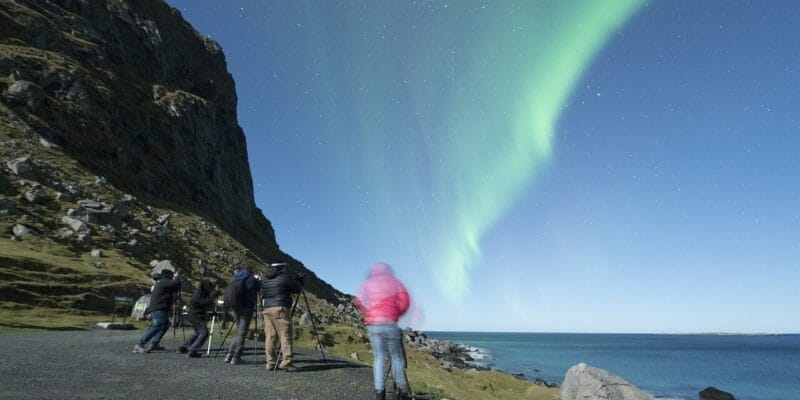 Nacht der Polarlichter Fotografen auf den Lofoten filmen das grüne Naturschauspiel der Polarlichter, ausgelöst durch Sonnenaktivität , während die Berge nahe Tromsø im Hintergrund aufragen.